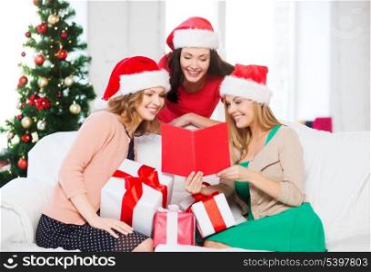 christmas, x-mas, winter, happiness concept - three smiling women in santa helper hats with card and many gift boxes