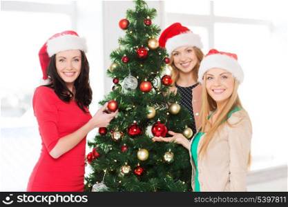 christmas, x-mas, winter, happiness concept - three smiling women in santa helper hats decorating a christmas tree