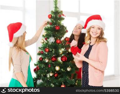 christmas, x-mas, winter, happiness concept - three smiling women in santa helper hats decorating a christmas tree
