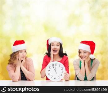 christmas, x-mas, winter, happiness concept - three smiling women in santa helper hats with clock showing 12