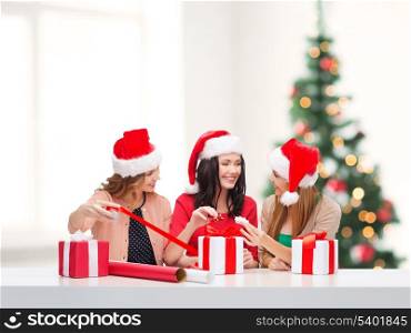 christmas, x-mas, winter, happiness concept - three smiling women in santa helper hats with gift boxes and wrapping paper