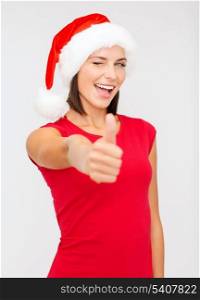 christmas, x-mas, winter, happiness concept - woman in santa helper hat showing thumbs up