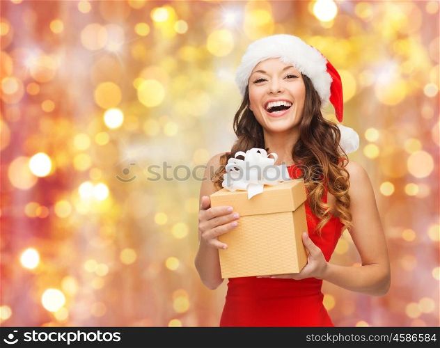 christmas, x-mas, winter, people and celebration concept - laughing woman in santa hat and red dress with gift box over holidays lights background