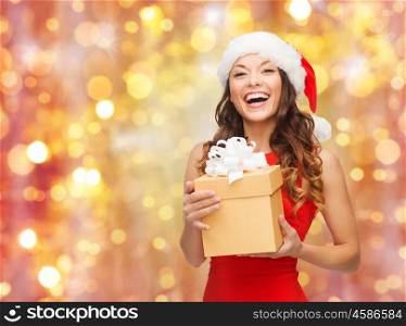christmas, x-mas, winter, people and celebration concept - laughing woman in santa hat and red dress with gift box over holidays lights background