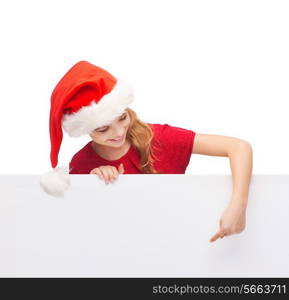 christmas, xmas, holidays and advertisement concept - happy girl child in santa helper hat pointing finger on blank white board