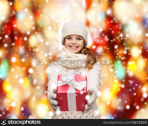 christmas, xmas, winter, happiness concept - smiling girl in hat, muffler and gloves with gift box
