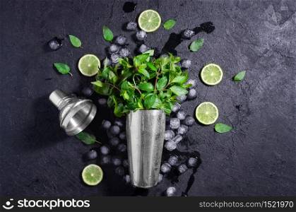Chrome Bar Shaker With Lime, Mint and Ice on Dark Stone Table. Concept Of Cold Summer Drinks. Top View Flat Lay. Copy Space For Your Text.. Chrome Bar Shaker With Lime, Mint and Ice on Dark Stone Table. Concept Of Cold Summer Drinks. Top View Flat Lay. Copy Space For Your Text