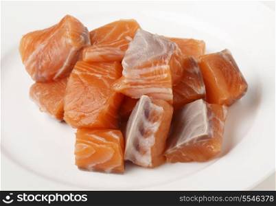 Chucks of salmon, cut from a fresh fillet, on a white plate in preparation for cooking