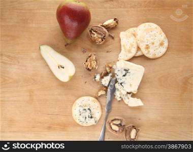 chunk of blue cheese with crackers, pear and walnuts on a cutting board