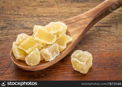 chunks of crystalised ginger on a wooden spoon against grunge wood background