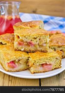 Chunks of sweet cake with rhubarb in a bowl, a jug of juice, napkin on a wooden boards background