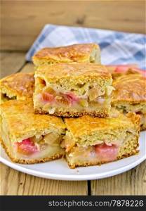 Chunks of sweet cake with rhubarb in a plate, napkin on a wooden boards background