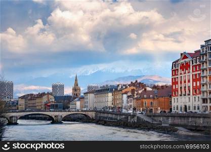 Church, Isere river and bridge in Grenoble, France. Scenic view of the banks of the Isere river and bridge, Collegiate Church of Saint-Andre with French Alps on the background, Grenoble, France