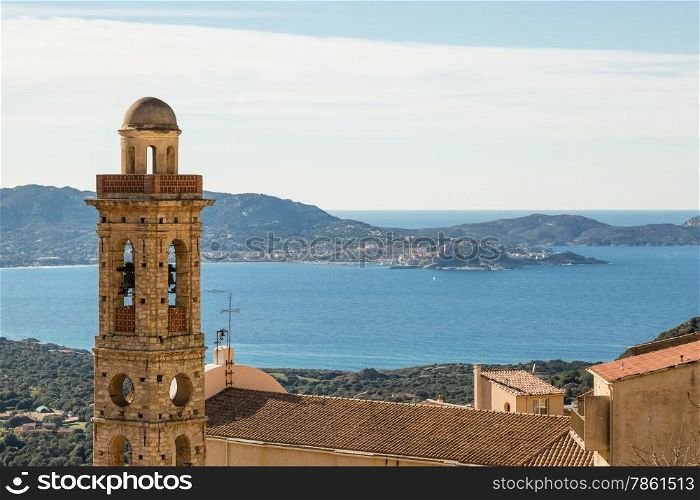 Church tower in the village of Lumio in the Balagne region of north Corsica with the mediterranean and the citadel of Calvi in the distance