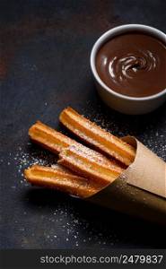 Churros in paper bag with sugar and chocolate sauce on dark black background