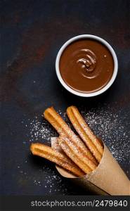 Churros in paper bag with sugar powder and chocolate sauce dip on dark black background