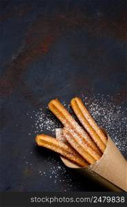 Churros sticks fresh hot in paper bag on dark background top view with copy space