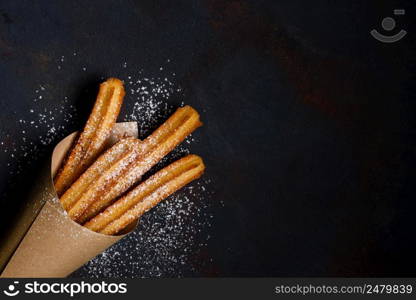 Churros sticks fresh hot in paper bag on dark background with copy space
