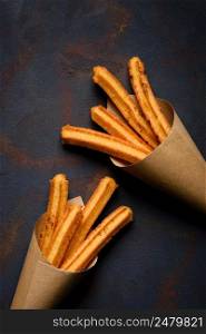 Churros sticks fresh hot with cinnamon in paper bag on dark background top view