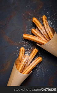 Churros sticks fresh hot with sugar powder and cinnamon in paper bag on dark background top view