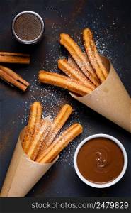 Churros with sugar powder with chocolate sauce dip and cinnamon sticks on dark background top view