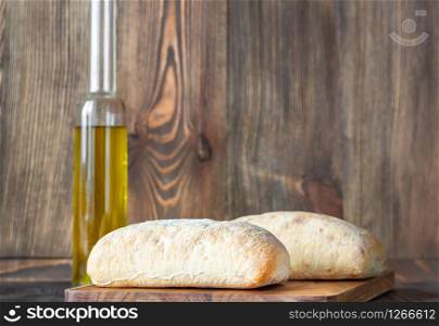 Ciabatta - Italian white bread with a glass bottle of olive oil on wooden background