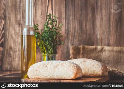 Ciabatta - Italian white bread with a glass bottle of olive oil on wooden background