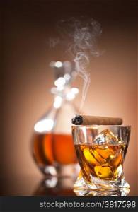 Cigar on glass with whiskey on brown background