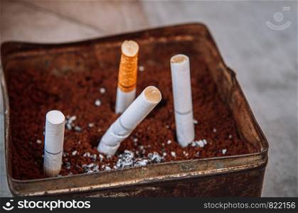 Cigarette filter in old dirty metal ashtray close up selective focus blurry background - Quit smoking concept
