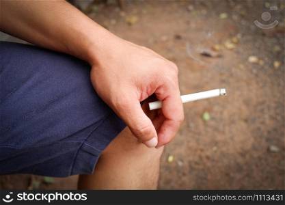 Cigarette smoke burning on hand man smoking on outdoors background