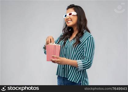 cinema and people concept - happy smiling asian woman in 3d movie glasses eating popcorn from striped bucket over grey background. asian woman in 3d movie glasses eating popcorn