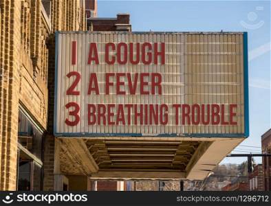 Cinema billboard with three main symptoms or signs of a coronavirus or Covid-19 infection of coughing, feverish and trouble with breathing. Symptoms of Coronavirus infection on downtown Main Street cinema