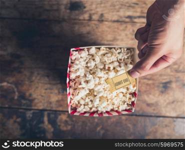 Cinema concept of hand holding movie ticket above a box of popcorn