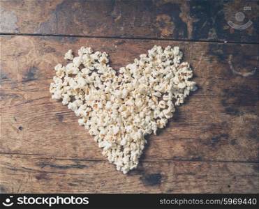 Cinema concept of popcorn arranged in a heart shape on wooden table