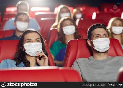 cinema, entertainment and pandemic concept - people wearing face protective medical masks for protection from virus disease watching movie in theater. people in masks watching movie in theater