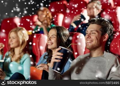 cinema, entertainment and people concept - happy friends with popcorn and lemonade drinks watching movie in theater with snowflakes