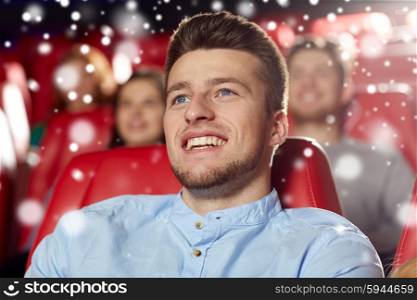 cinema, entertainment and people concept - happy young man watching comedy movie in theater with snowflakes