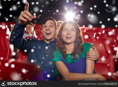 cinema, entertainment, gesture, emotions and people concept - happy couple watching movie pointing finger to screen in theater with snowflakes