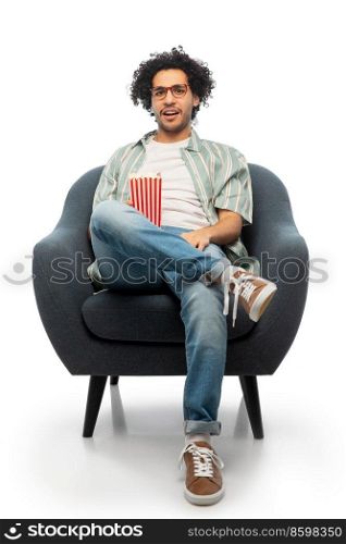 cinema, leisure and entertainment concept - displeased man with popcorn watching movie sitting in chair over white background. man with popcorn watching movie sitting in chair