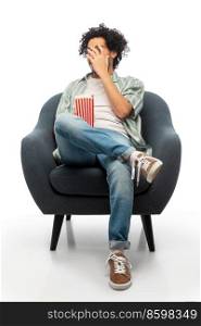 cinema, leisure and entertainment concept - scared man with popcorn watching movie sitting in chair over white background. man with popcorn watching movie sitting in chair