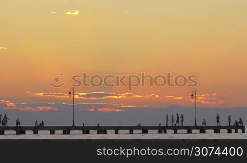 Cinemagraph - People fishing and looking at sea from the pier, lonely seagull flying over them. Scenic sunset with clouds in golden sunlight