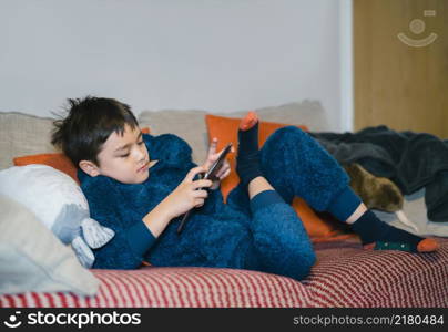 Cinematic portrait happy kid watching cartoon on tablet, Candid shot cute boy playing game online with friends on internet, Cozy Child wearing fluffy pajamas sitting on sofa relaxing at home