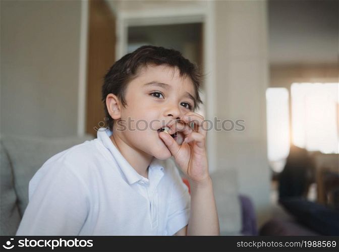 Cinematic portrait young boy looking out deep in thought while eating nut, Happy Child sitting alone with thinking face, Kid relaxing at home after back from school.