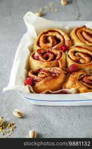 Cinnabon buns. Sinabon rolls with cream cheese, cream and brown sugar on grey background. Cinnamon rolls with raspberries and pistachios