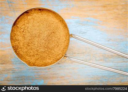cinnamon (cassia) bark powder in a metal measuring scoop against painted wood