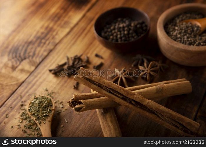 Cinnamon sticks and various spices on wooden rustic board background. Pepper, cardamom, clove, star anis, dehydrated parsley. Close up