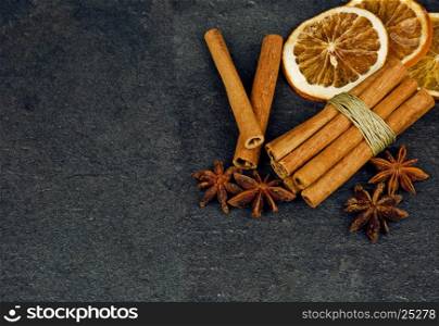 Cinnamon sticks, star anise and two slices of dried orange on a dark, stone table, as a Christmas decoration. Flat, top, horizontal view.