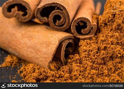 cinnamon sticks with powder on dark stone plate