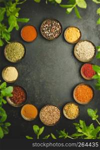 Circle frame composition of spices and herbs over dark background - flat lay. Various bowls of spices over dark background