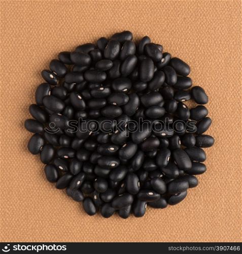 Circle of black beans on brown vinyl background.